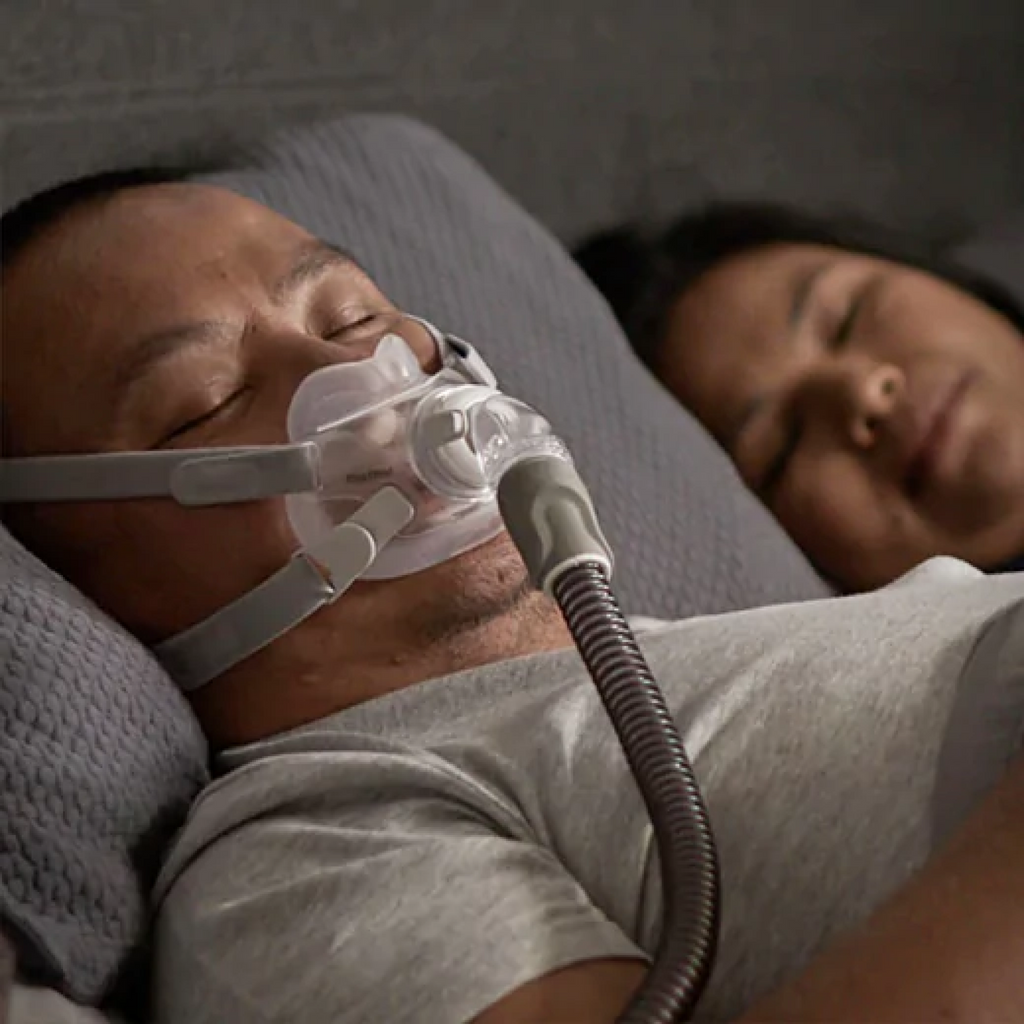 Man sleeping with a ResMed AirFit F30 CPAP mask on his face next to a partner.