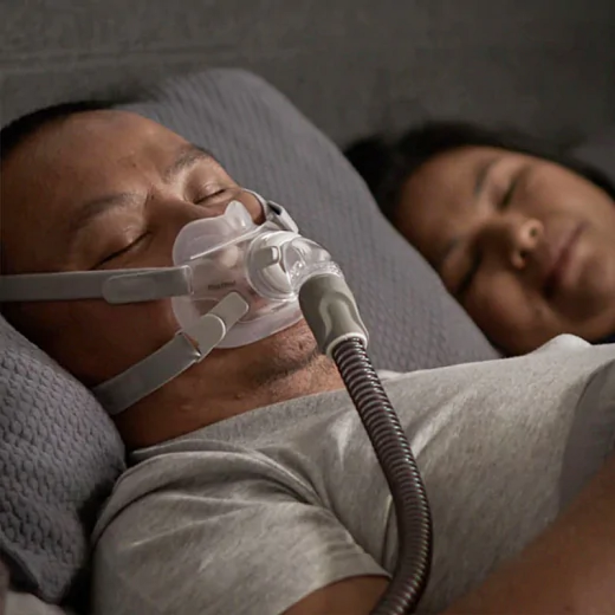 Man sleeping with a ResMed AirFit F30 CPAP mask on his face next to a partner.