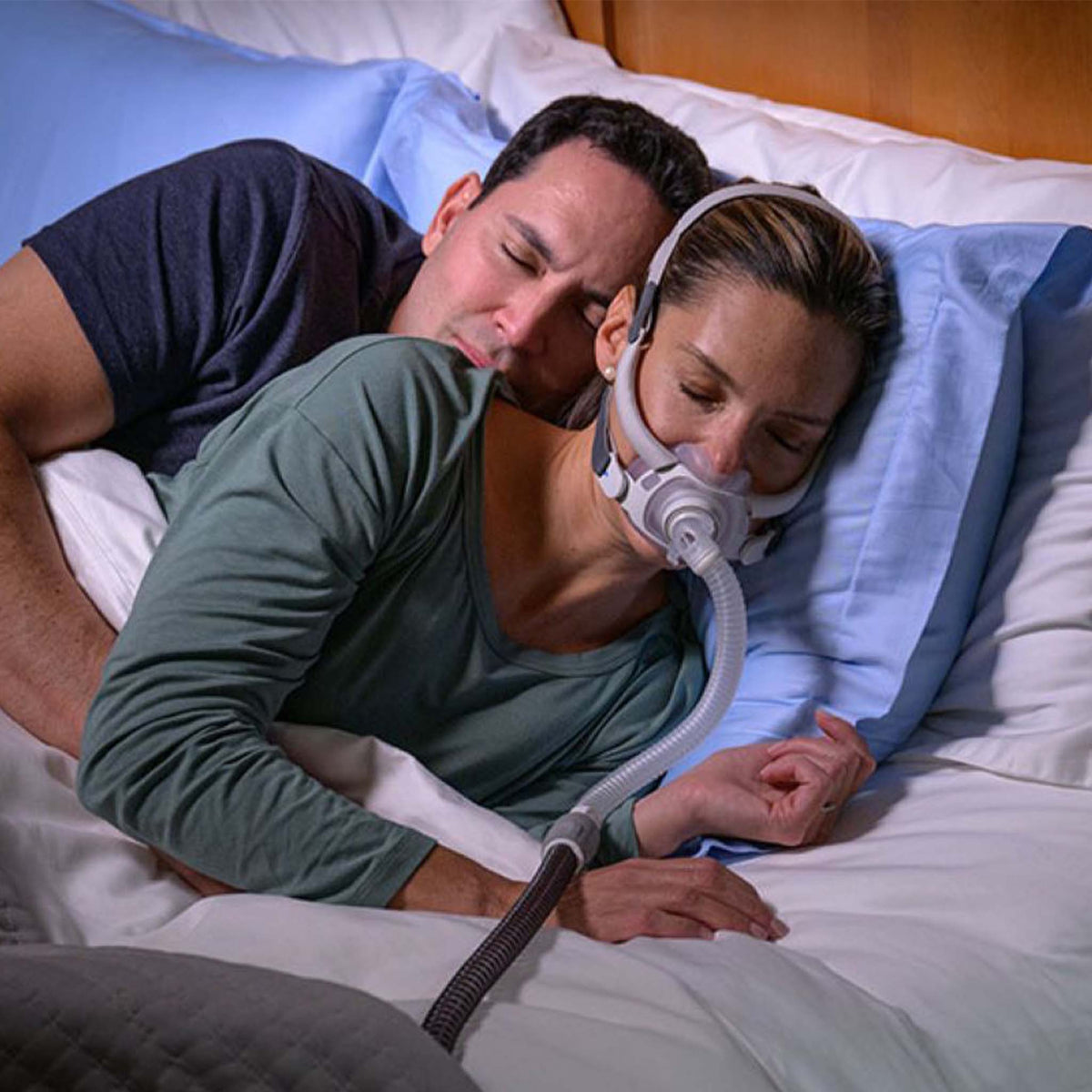 Woman sleeping in bed wearing a ResMed AirFit F40 full face CPAP mask next to her partner.