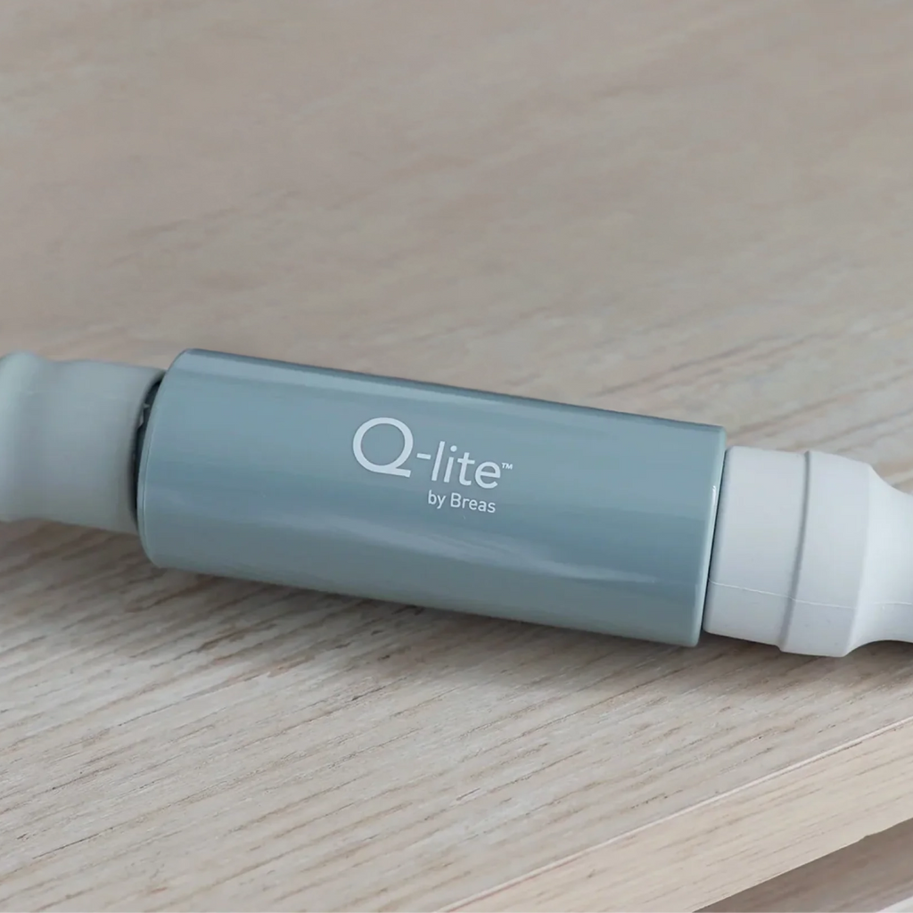 Q-lite by Breas noise cancelling device, light blue cylindrical body, side view on wooden surface