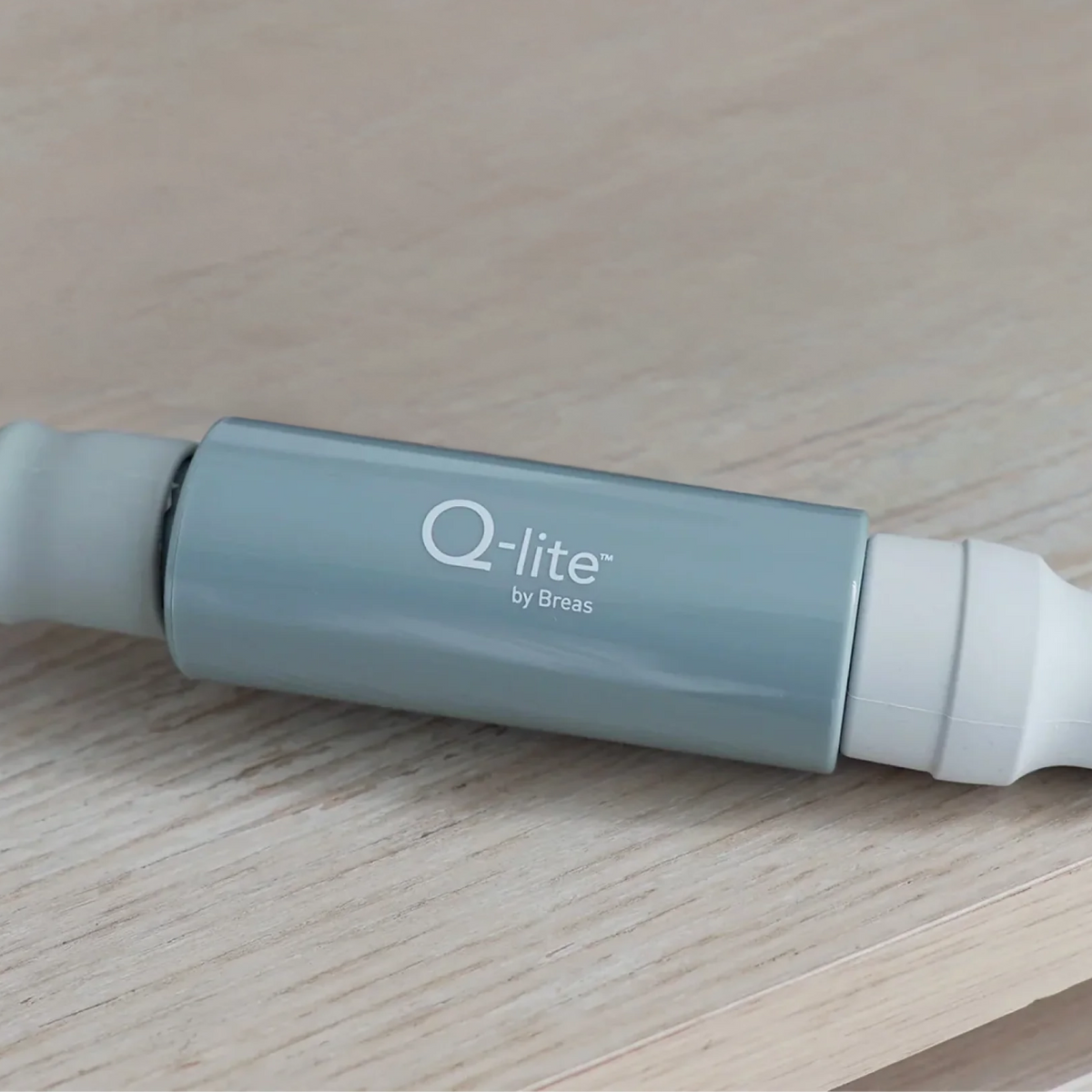 Q-lite by Breas noise cancelling device, light blue cylindrical body, side view on wooden surface