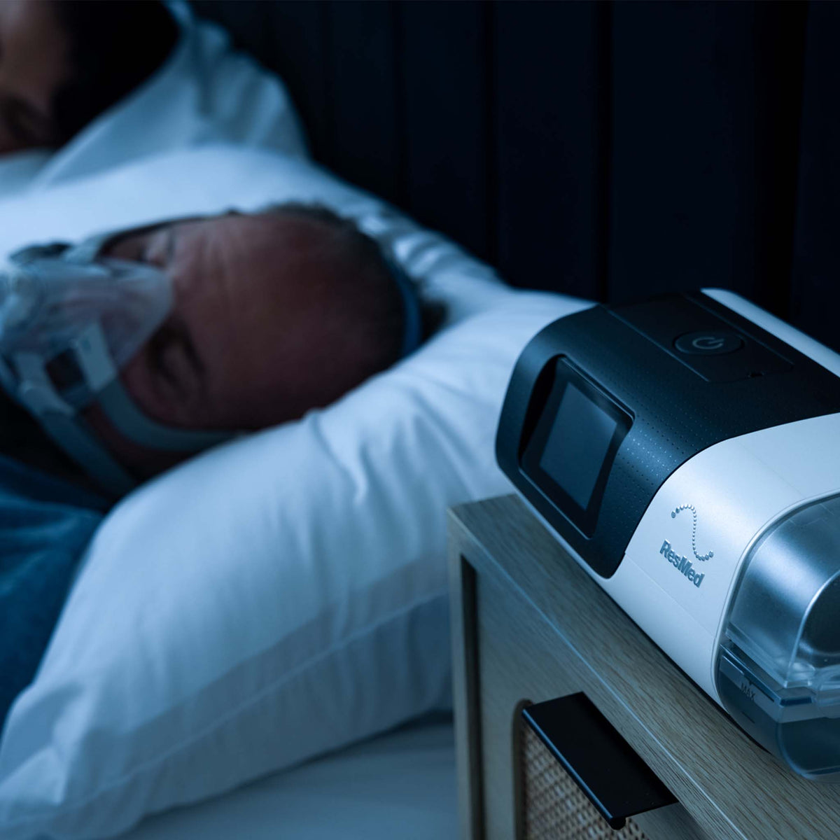 Person sleeping with ResMed AirFit F20 mask and AirSense 11 machine on a bedside table.
