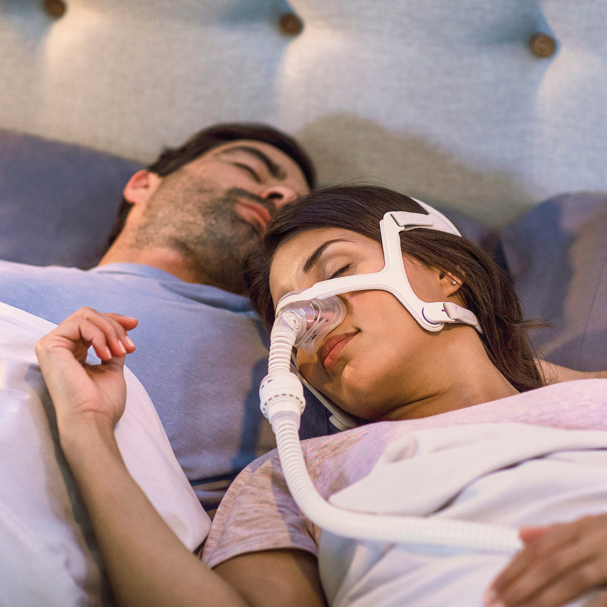 Woman sleeping in bed wearing a ResMed AirFit N20 nasal CPAP mask beside her partner.