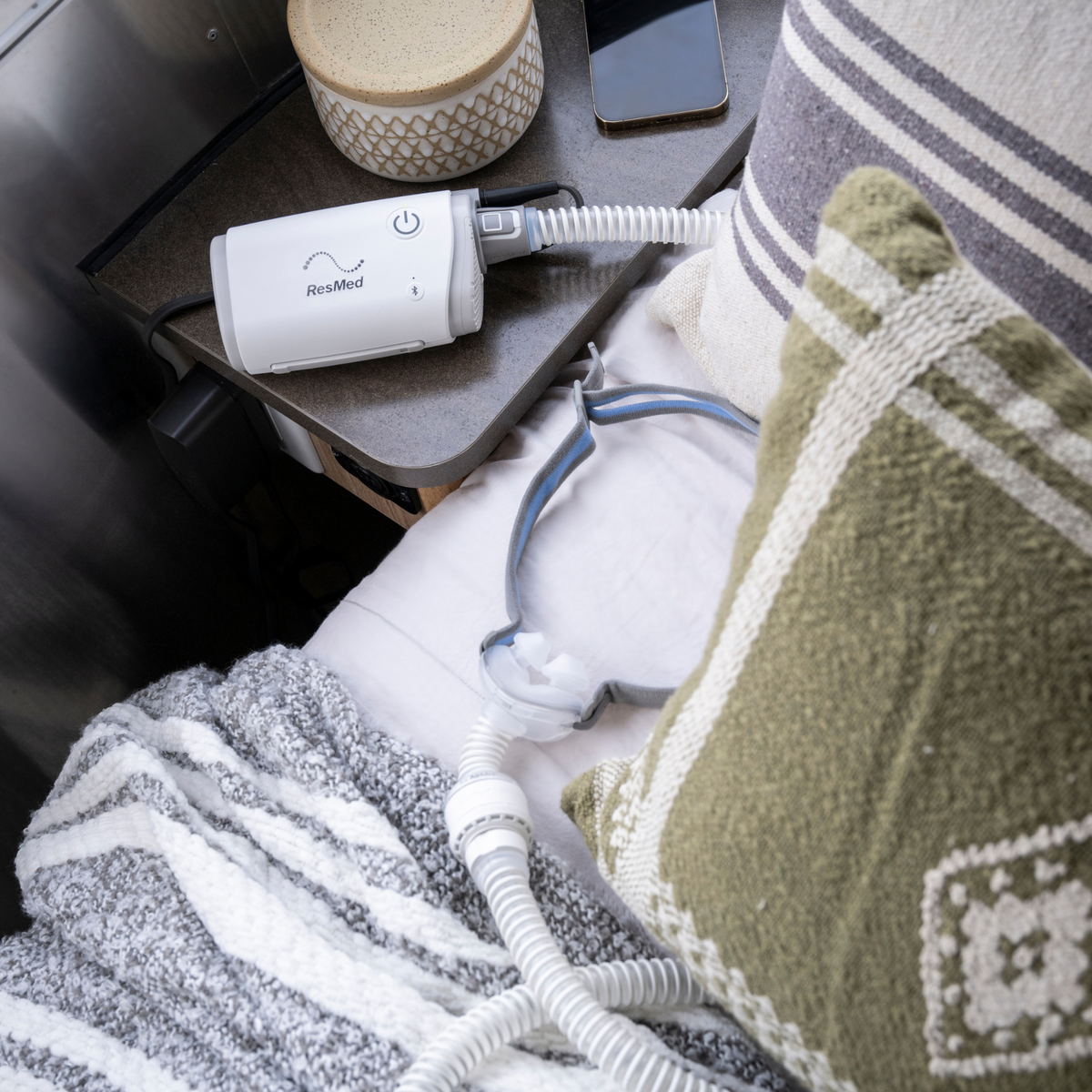 ResMed AirMini CPAP machine and AirFit P10 mask on a bedside table next to a pillow.