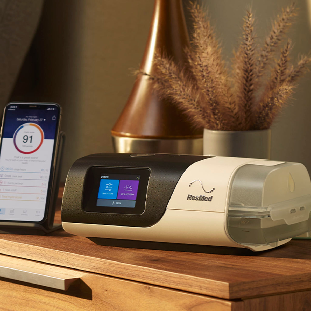 ResMed AirSense 11 CPAP machine on a wooden bedside table next to a smartphone displaying sleep data.