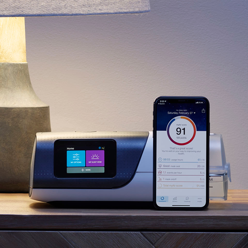 ResMed AirSense 11 CPAP machine on a bedside table next to a smartphone displaying sleep data.