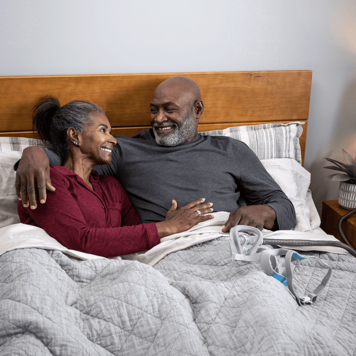 A smiling senior couple in bed with a ResMed AirTouch F20 CPAP mask resting on the grey bedding.